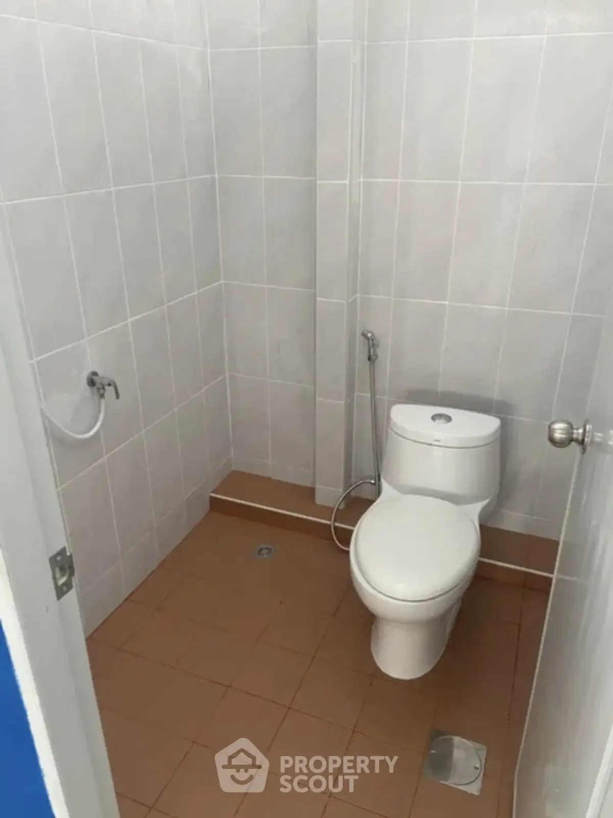 Compact bathroom with tiled walls and floor, featuring a modern toilet and bidet spray.