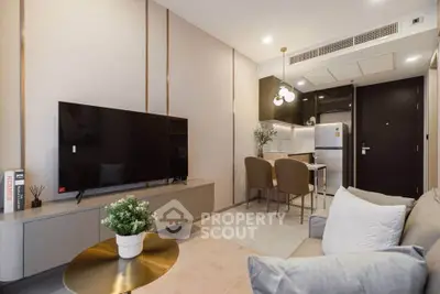 Modern living room with sleek furniture and open kitchen layout, featuring a large TV and stylish decor.