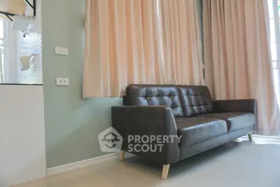Modern living room with elegant dark leather sofa, pastel curtains, and ample natural light, perfect for relaxation and social gatherings.