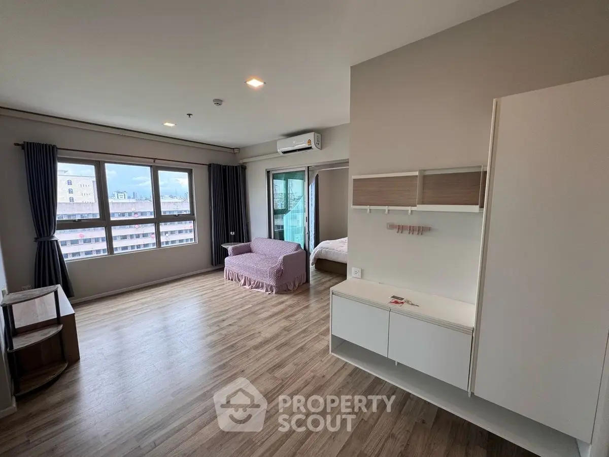 Spacious studio apartment with modern decor and large windows offering city views.