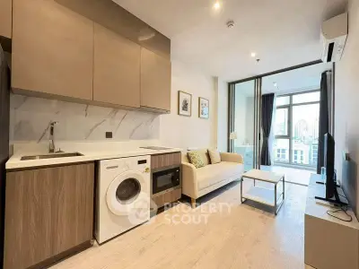 Modern open-plan living room with kitchen, featuring washing machine and city view.