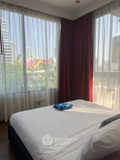 Modern bedroom with large windows and city view, featuring elegant red curtains and a cozy bed.