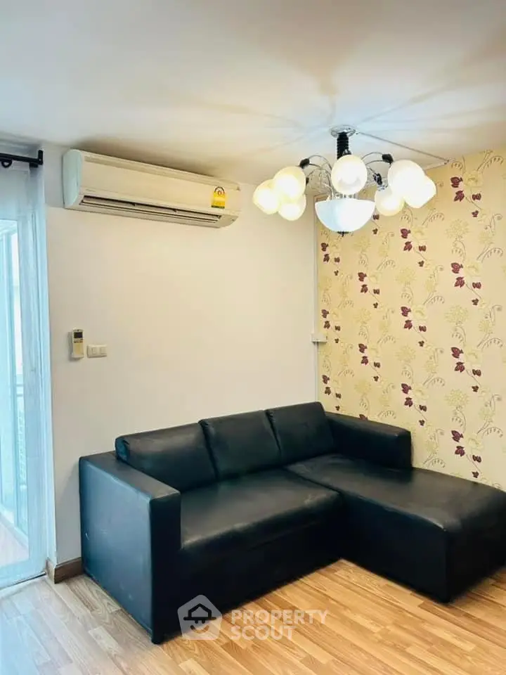 Cozy living room with modern black sofa and stylish lighting, featuring floral accent wall and wooden flooring.