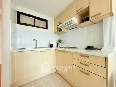 Modern kitchen with light wood cabinets and sleek appliances in a cozy corner layout.