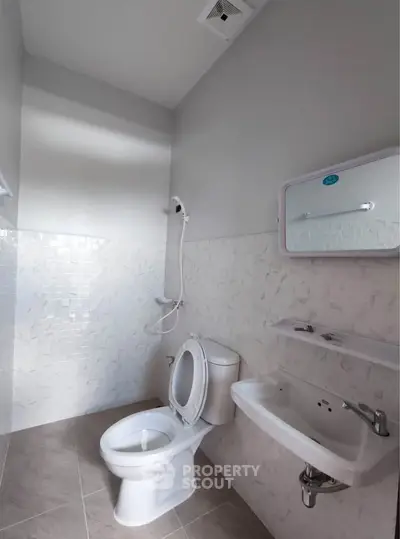 Modern bathroom with sleek fixtures and neutral tiles, featuring a toilet, sink, and shower.