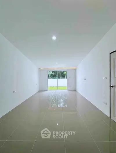 Spacious empty room with glossy tiled floor and large window overlooking garden.