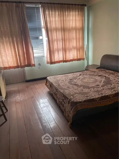 Cozy bedroom with wooden flooring and natural light through curtains.