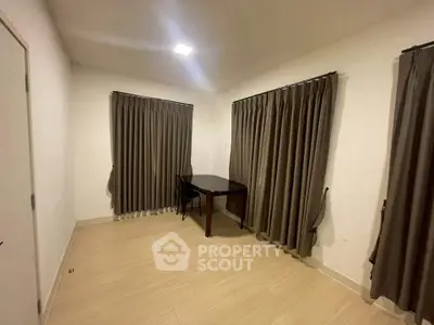 Spacious room with elegant curtains and wooden flooring, perfect for a cozy study or office setup.