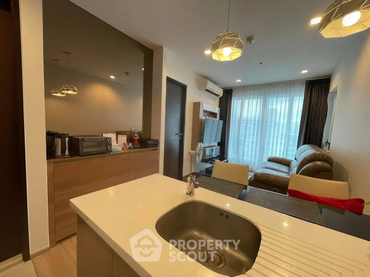 Modern living room with open kitchen, featuring stylish lighting and cozy seating area.