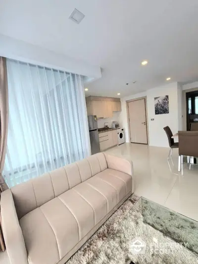 Modern open-plan living room with kitchen and dining area, featuring sleek furniture and natural light.