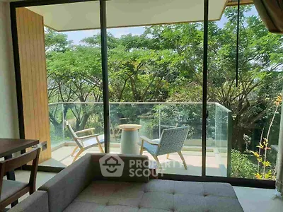 Serene living room with large glass doors opening to a lush balcony view, modern furniture, and abundant natural light.