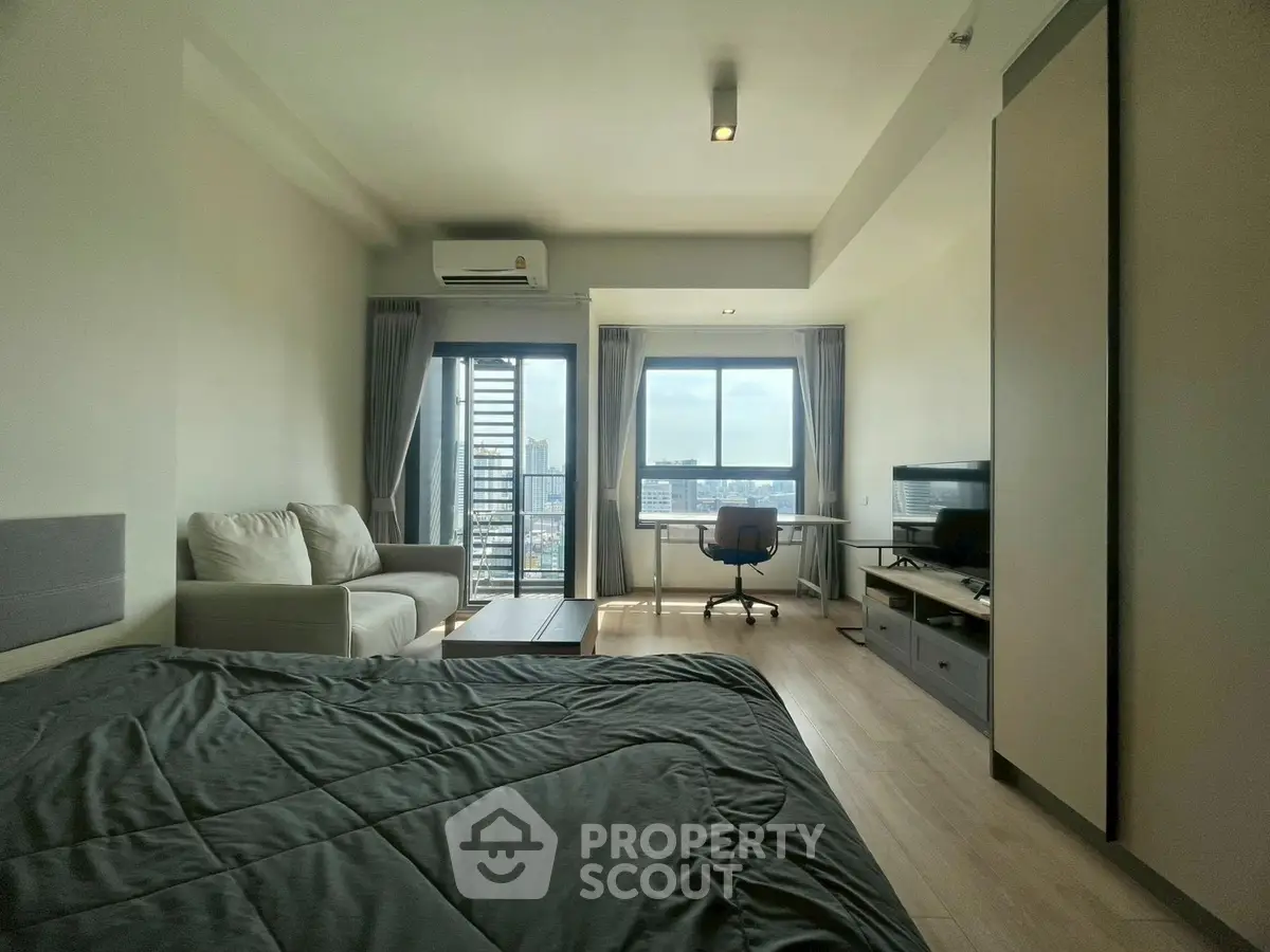 Modern bedroom with city view, cozy seating, and workspace in a stylish apartment.