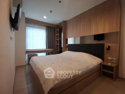 Modern bedroom with cozy bed, wall-mounted TV, and large window for natural light.