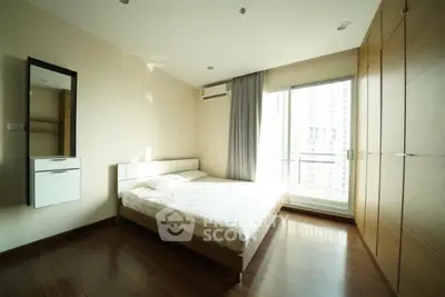 Spacious bedroom with large window and modern furnishings in high-rise apartment