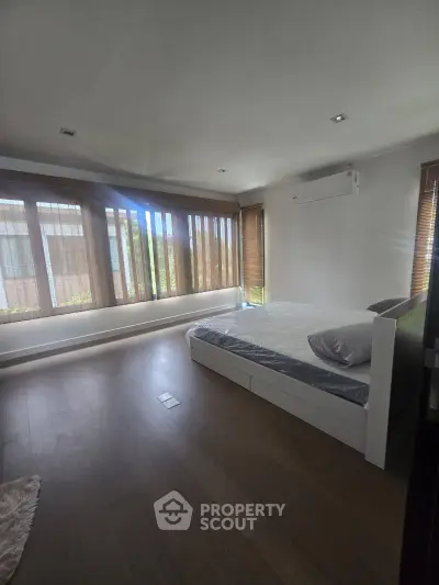 Spacious bedroom with large windows and modern decor, featuring hardwood floors and ample natural light.