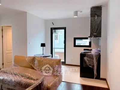 Modern living room with wrapped furniture and kitchen area, featuring sleek design and natural light.
