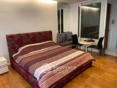 Modern bedroom with stylish decor and wooden flooring, featuring a cozy bed and a small dining area.