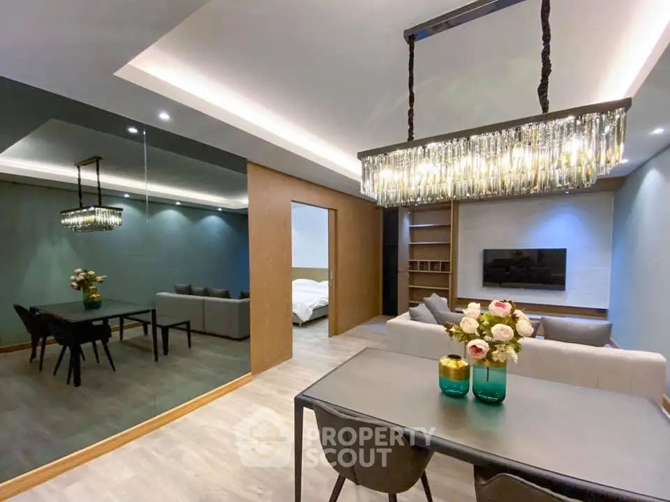 Modern living room with elegant chandelier and mirrored wall, open to dining area.