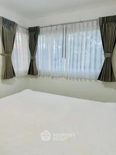 Cozy bedroom with large windows and elegant curtains, offering a bright and inviting atmosphere.