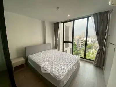 Modern bedroom with large windows offering city view in high-rise apartment.