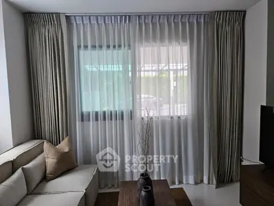 Elegant living room with modern decor and large window draped in sheer curtains.