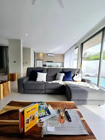 Modern living room with large gray sectional sofa, wooden coffee table, and pool view through glass doors.