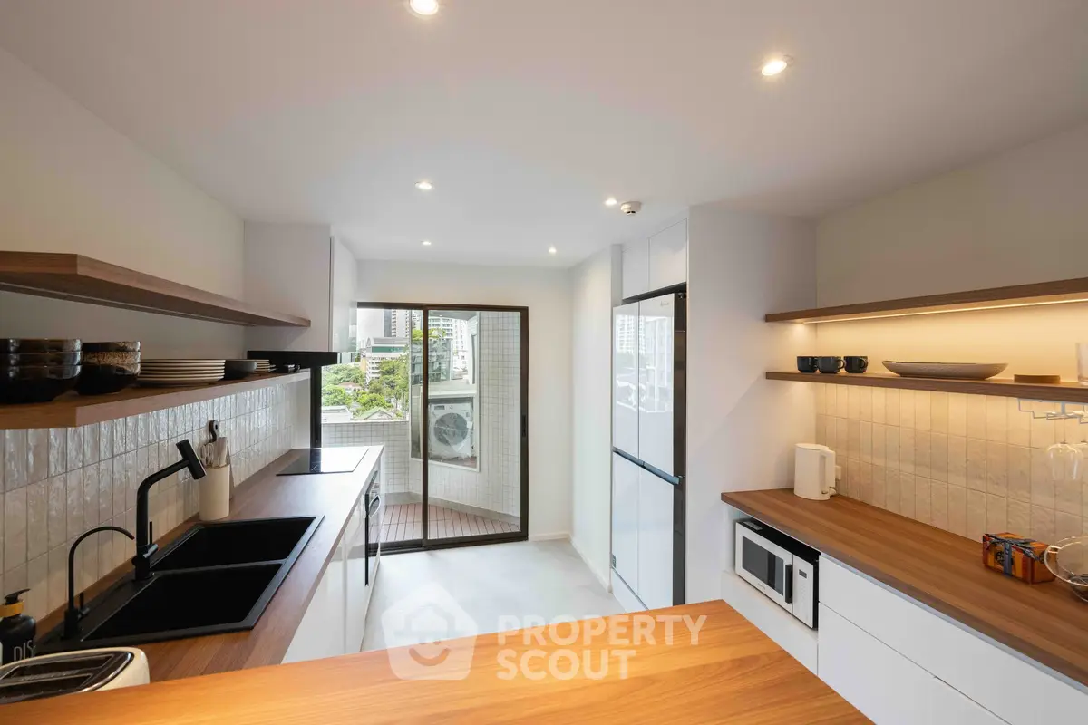 Modern kitchen with sleek wooden countertops and open layout, featuring city view from balcony.