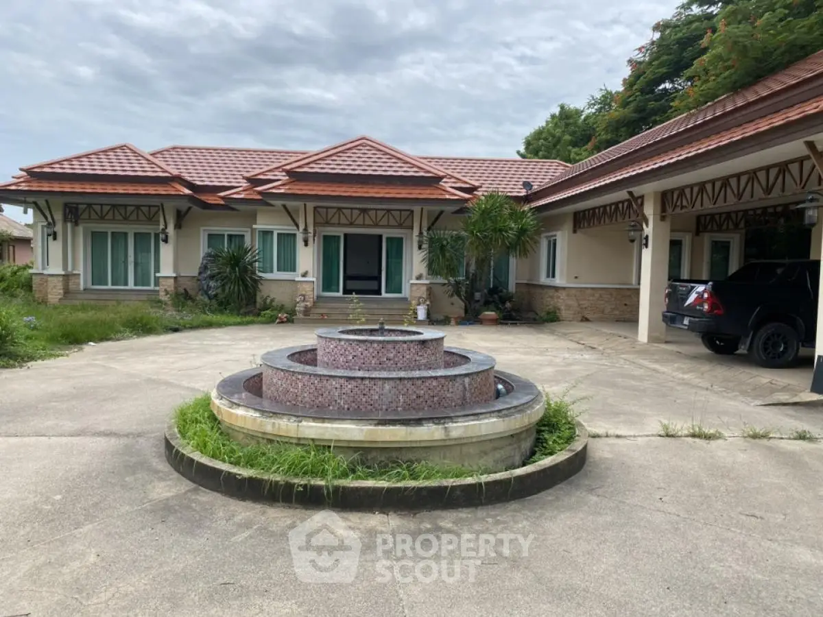 Spacious single-story home with circular driveway and fountain, featuring a covered carport and lush greenery.