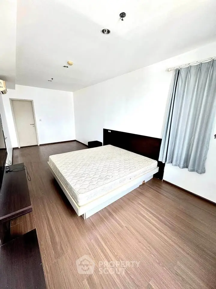 Spacious bedroom with wooden flooring and natural light