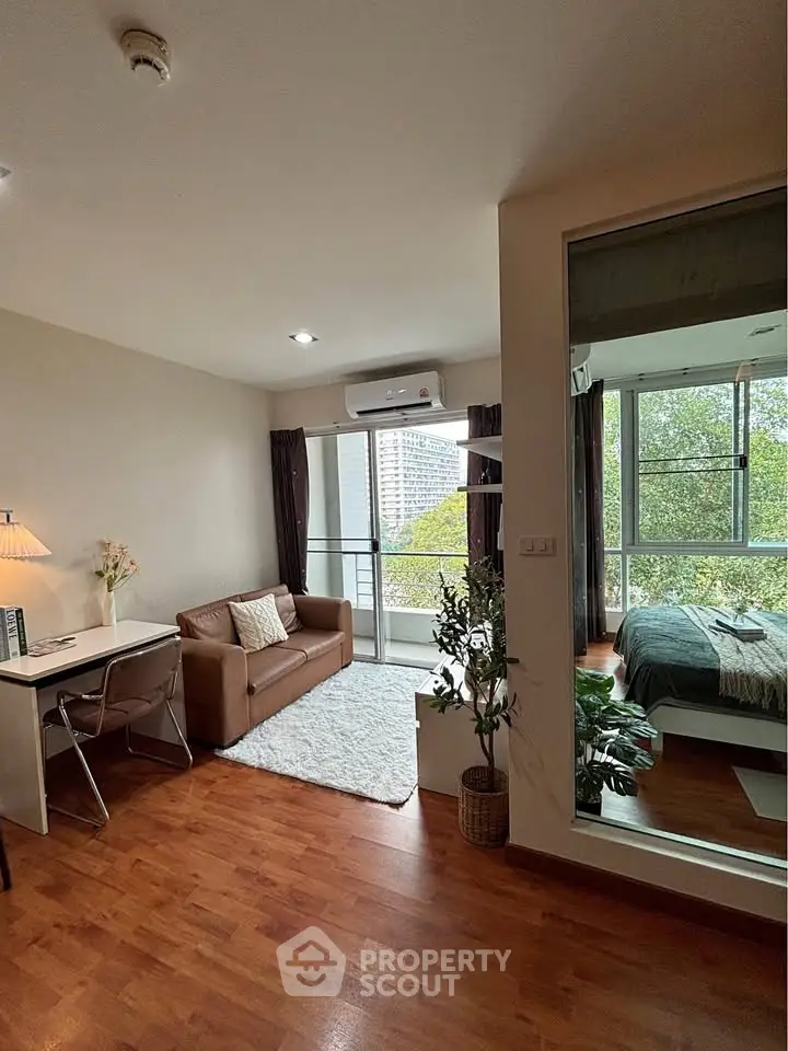 Modern apartment with open living room and bedroom, featuring hardwood floors and large windows with city view.