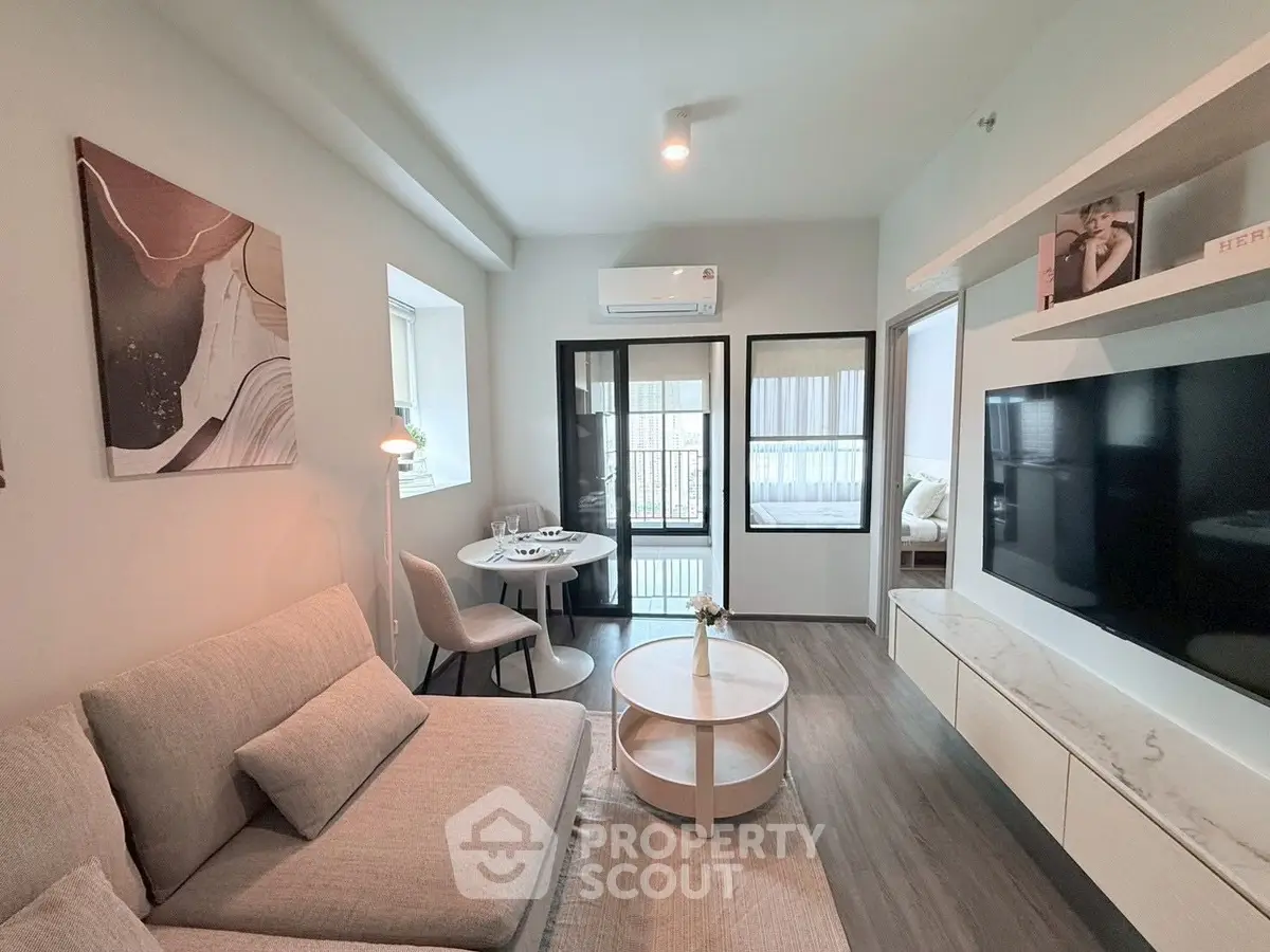 Modern living room with stylish decor and natural light, featuring a cozy seating area and large TV.