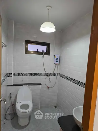Modern bathroom with sleek white tiles and compact design, featuring a shower and toilet.