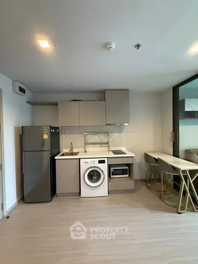 Modern kitchen with washing machine, fridge, and dining area in a compact apartment.
