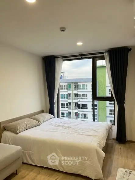 Cozy bedroom with large window offering a city view, featuring a comfortable bed and modern decor.