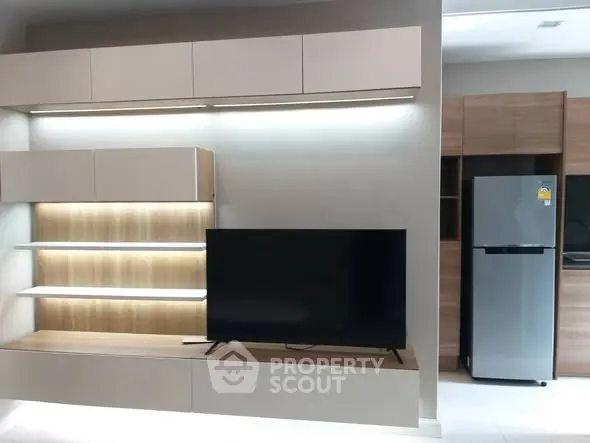 Modern living room with sleek TV unit and stainless steel fridge in open layout.