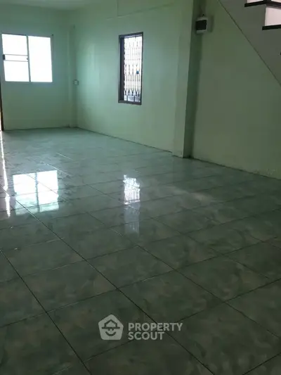 Spacious empty room with glossy tiled floor and staircase, ideal for customization.