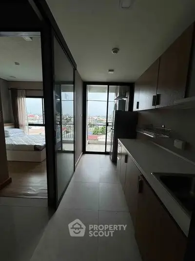 Modern apartment interior with sleek kitchen and bedroom view, featuring large windows and balcony access.