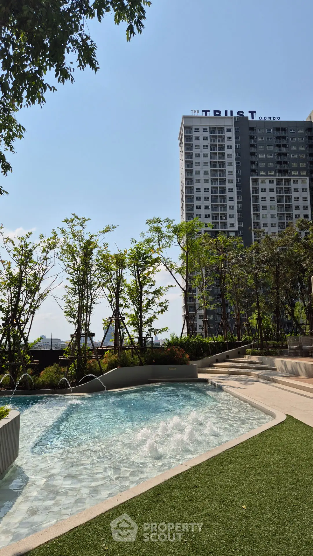 Modern condo building with lush garden and inviting pool area under clear blue sky.