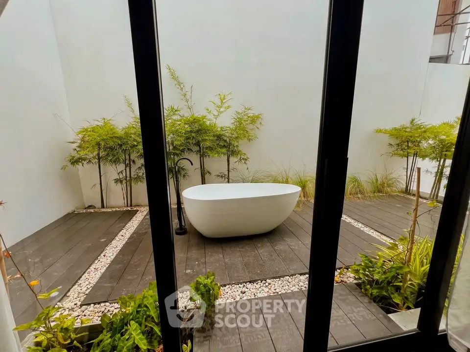 Modern outdoor patio with elegant standalone bathtub and lush greenery