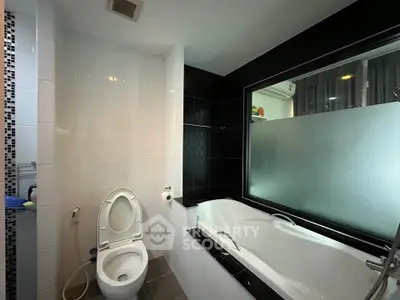 Modern bathroom with sleek black and white design featuring a bathtub and toilet.