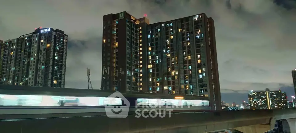 Stunning night view of modern high-rise buildings with city lights and passing train, perfect urban living.