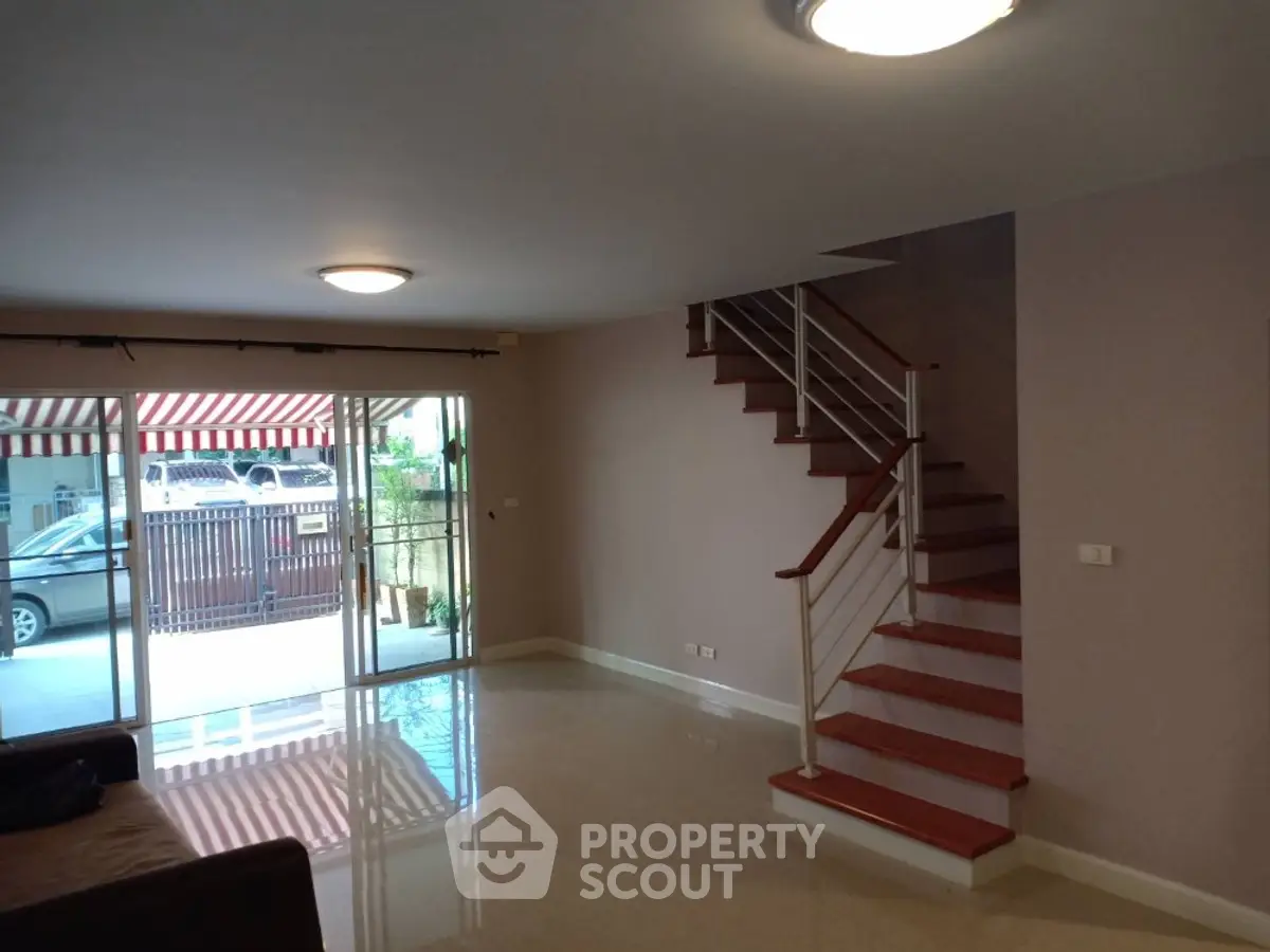 Spacious living room with modern staircase and large glass doors leading to outdoor area.