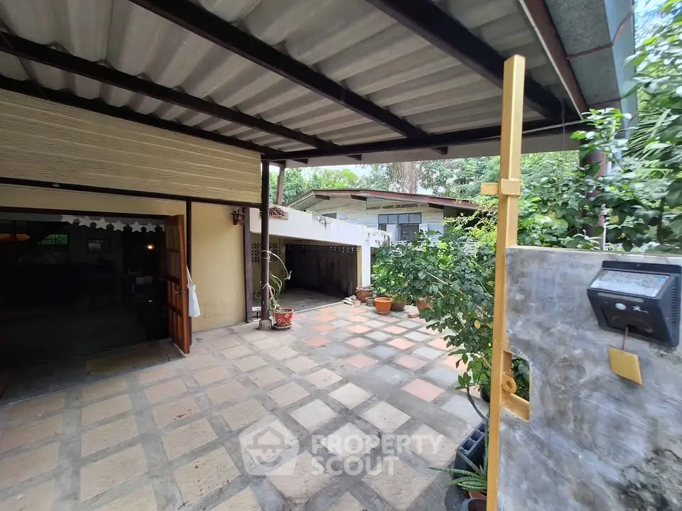 Charming outdoor patio with lush greenery and spacious tiled area, perfect for relaxation and entertaining.