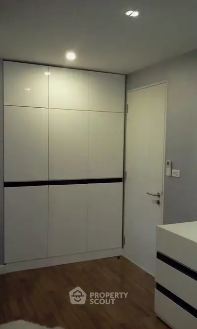 Modern minimalist bedroom with sleek white wardrobe and wooden flooring.
