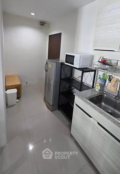 Modern kitchen with sleek cabinets, microwave, and refrigerator in a compact layout.