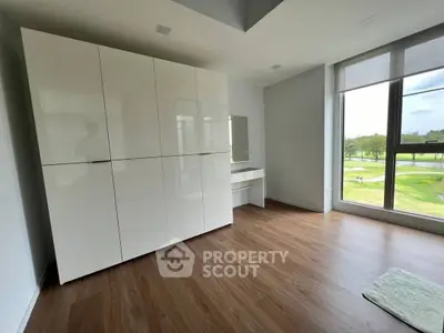 Spacious and modern living room with large windows offering ample natural light and a serene view, complemented by sleek white storage cabinets and warm wooden flooring.