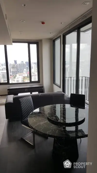 Modern living room with city view, featuring sleek black furniture and large windows.