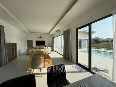 Luxurious open-plan living space with seamless indoor-outdoor flow, featuring large sliding glass doors leading to a sun-drenched pool area, modern furnishings, and a serene mountain backdrop.