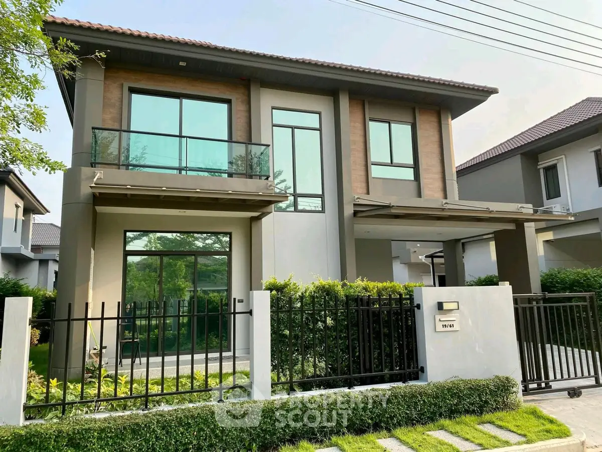 Modern two-story house with large windows and lush garden in a serene neighborhood.