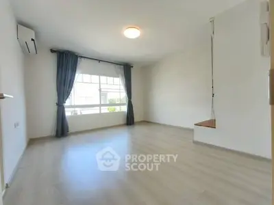 Spacious empty room with large window and wooden flooring, ideal for customization.